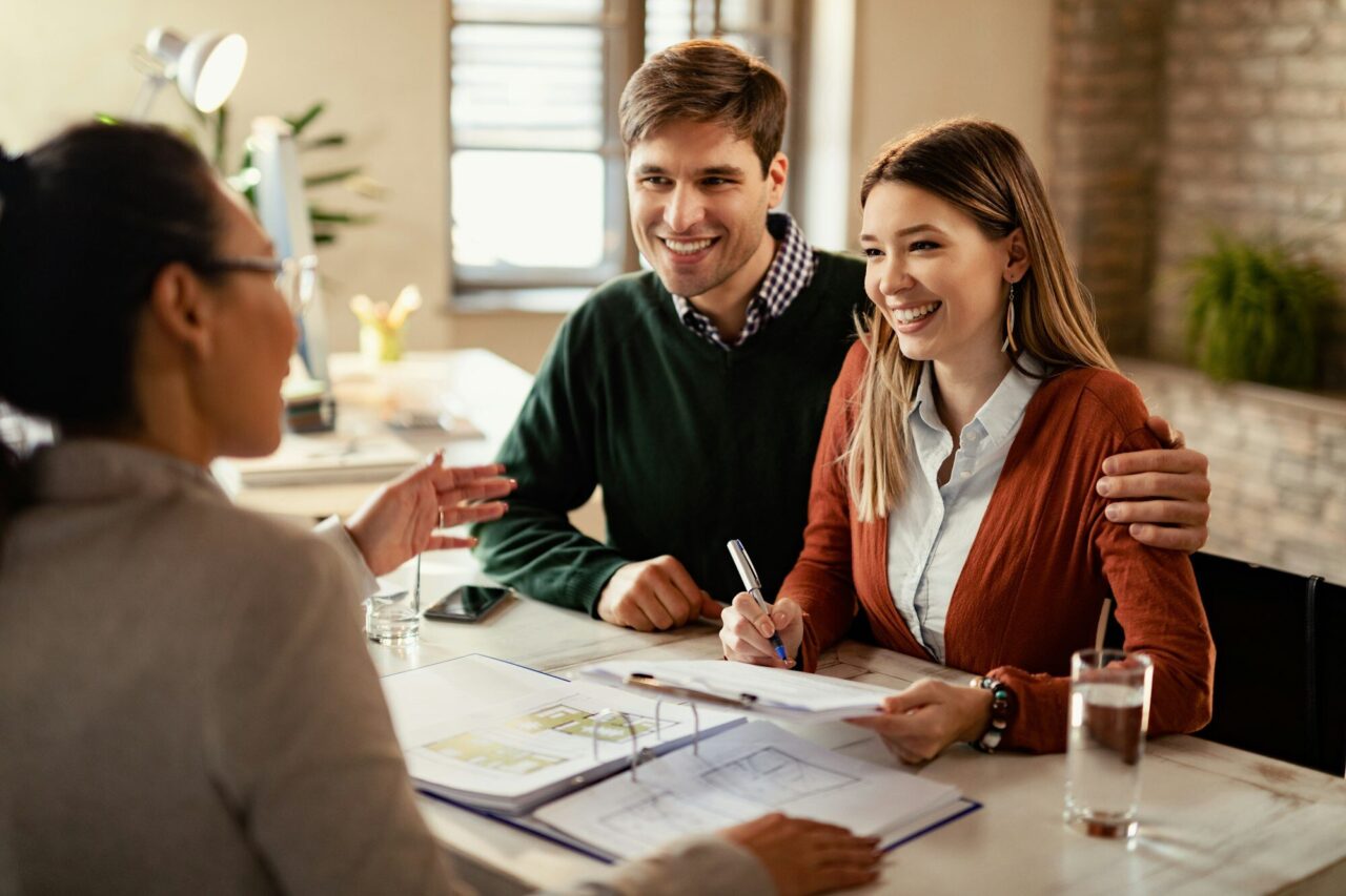 happy-couple-signing-mortgage-contract-while-having-meeting-with-real-estate-agent-